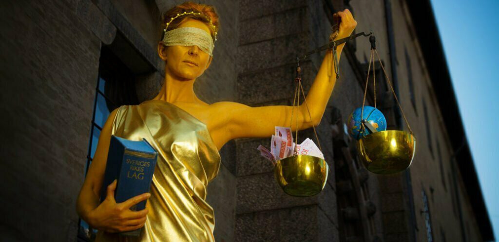 mänsklig konstinstallation av rättvisans gudinna Justitia utanför Stockholms tingsrätt med pengarna vs planeten i vågskålarna