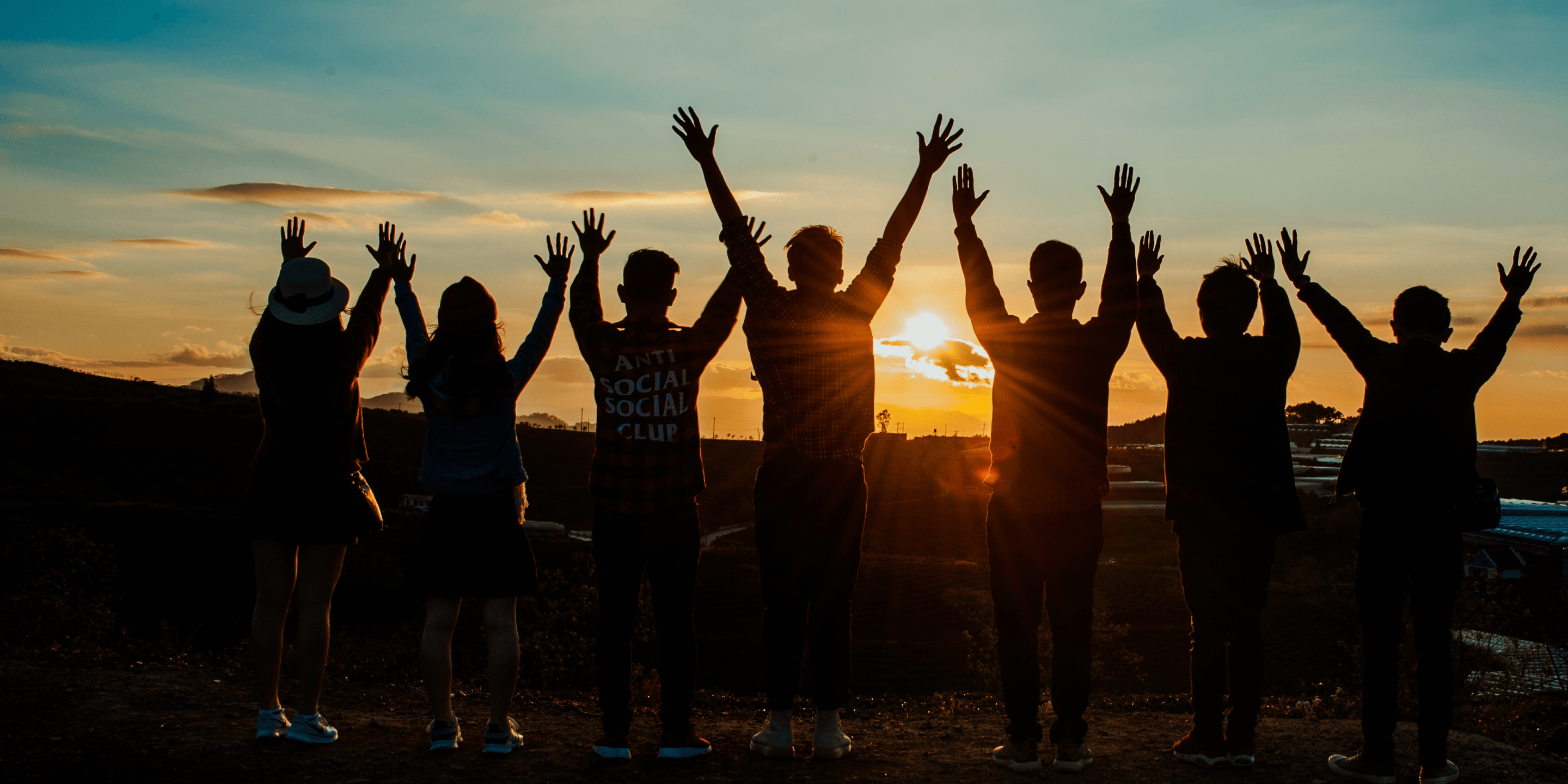 En grupp ungdomar sträcker armarna mot luften i en solnedgång