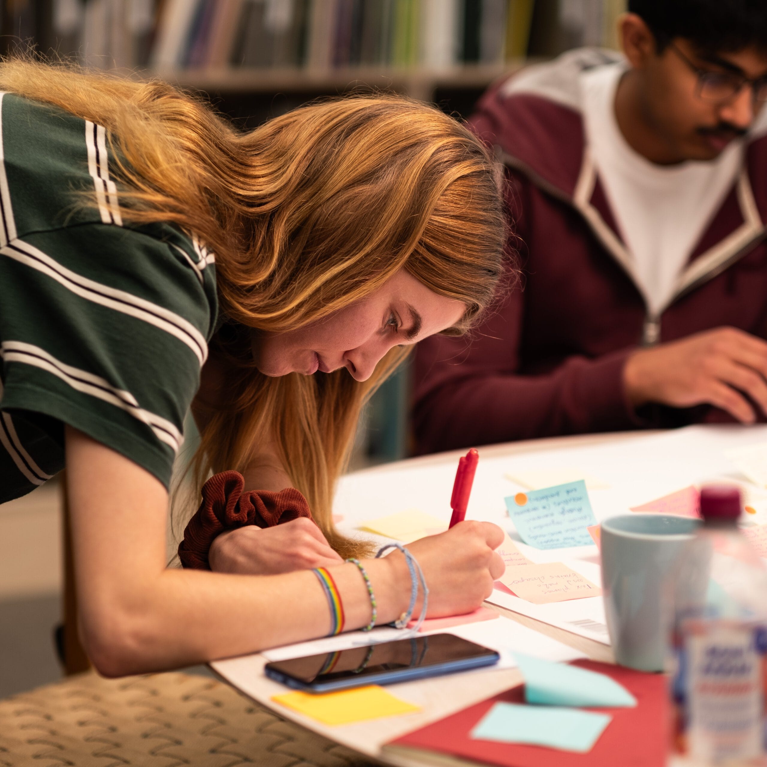 Ung person lutar sig fram över ett bord och skriver